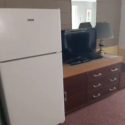 a white refrigerator next to a tv and a dresser at Alpine Lodge Motel & Restaurant in Grande Cache