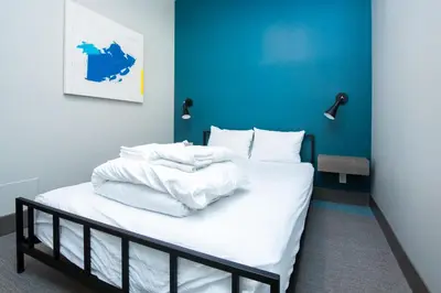 a bed with white sheets and a blue wall at Nowhere Special Hostel in Rossland