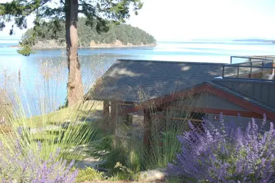 a house on the shore of a lake with purple flowers at Mayne Island Resort in Mayne Island