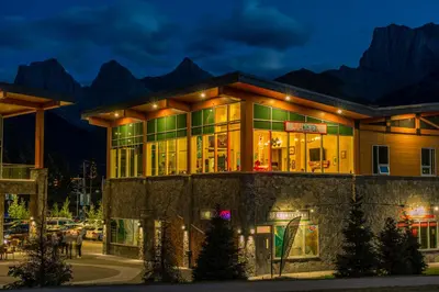 a building with lights on in front of mountains at Canmore Downtown Hostel in Canmore
