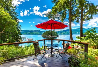 a deck with a table and chairs and an umbrella at Tranquility Bay Waterfront Inn in Sechelt
