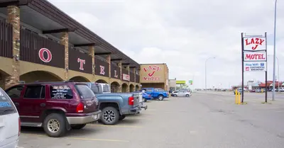 a parking lot with cars parked in front of a motel at Lazy J Motel in Claresholm