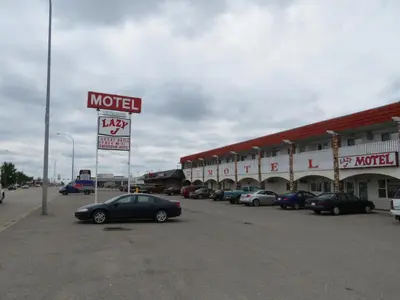 a motel with cars parked in a parking lot at Lazy J Motel in Claresholm