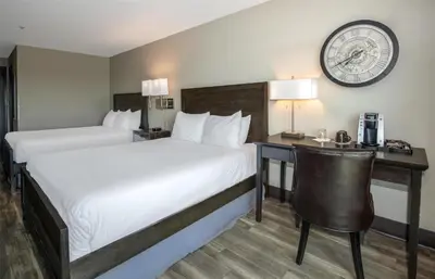 a hotel room with two beds and a desk and a clock at Coast Lonsdale Quay Hotel in North Vancouver