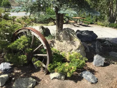 a garden with a rusty wheel and rocks and a picnic table at Riverside Motel Cache Creek in Cache Creek