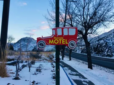 a sign for a motel with a red car at Riverside Motel Cache Creek in Cache Creek