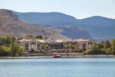 a building on the shore of a lake with a boat at Walnut Beach Resort in Osoyoos