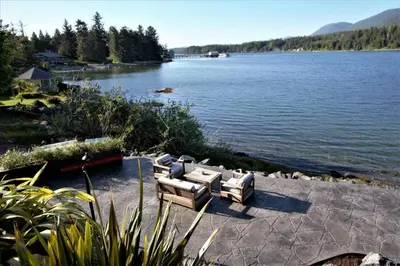 a couple of couches sitting on a patio next to a lake at Waterfront Hot Tub Firepit King Bed - 6H in Ucluelet