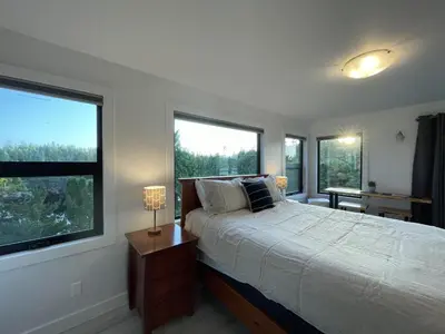 a bedroom with a bed and two large windows at Waterfront Private Room With Hot Tub & Firepit in Ucluelet
