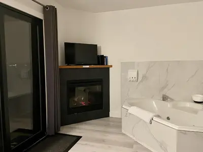 a bathroom with a fireplace and a tub and a tv at Waterfront Private Room With Hot Tub & Firepit in Ucluelet