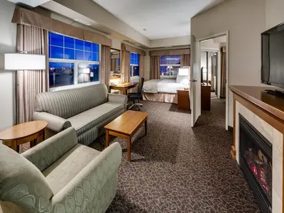 a hotel room with a couch and a bed and a fireplace at Heritage Inn & Suites - Brooks in Brooks