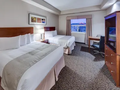 a hotel room with two beds and a desk at Heritage Inn & Suites - Brooks in Brooks