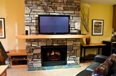 a living room with a stone fireplace with a flat screen tv at Pinnacle Ridge Chalets by Fernie Lodging Co in Fernie