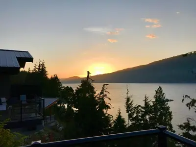 a sunset over a body of water with trees and a house at Port Renfrew Vacation Rentals in Port Renfrew