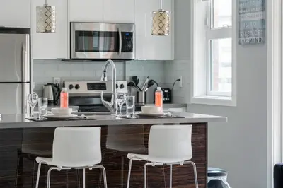 a kitchen with a counter with three white bar stools at ELEMENT ON FIRST by Manna in Calgary