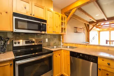 a kitchen with wooden cabinets and a stove and microwave at 3 BR 3 Bath ski in ski out with private hot tub in Big White