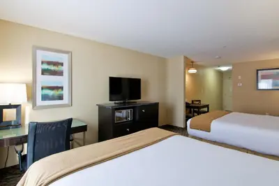 a hotel room with two beds and a desk and a tv at Wingate by Wyndham Fort Saskatchewan in Fort Saskatchewan