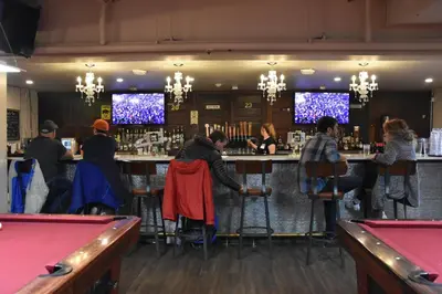 a group of people sitting at a bar with pool tables at PARTY HOSTEL - The Canmore Hotel Hostel in Canmore