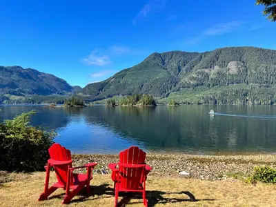 two red chairs sitting on the shore of a lake at Frigon Suite -Waterfront in Port Alice