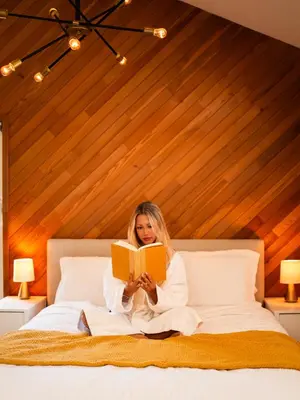 a woman sitting on a bed reading a book at Mid-Island Getaway - Sunken Hot Tub & Deck - Close to Beach - Modern in Nanaimo