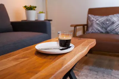 a cup of coffee on a wooden table with a spoon at Mid-Island Getaway - Sunken Hot Tub & Deck - Close to Beach - Modern in Nanaimo
