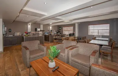 a living room with chairs and tables and a kitchen at Coast Fort St John Hotel in Fort Saint John