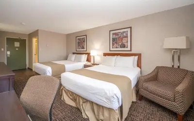 a hotel room with two beds and a chair at Coast Fort St John Hotel in Fort Saint John