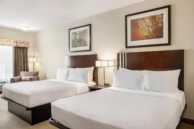a hotel room with two beds and a chair at Ramada by Wyndham Lac La Biche in Lac La Biche