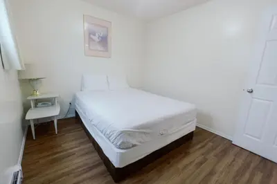 a white bedroom with a bed and a table at Beachside Motel in Penticton