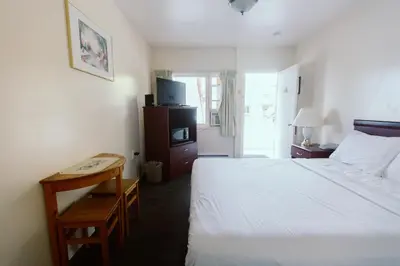 a bedroom with a white bed and a table and a desk at Beachside Motel in Penticton
