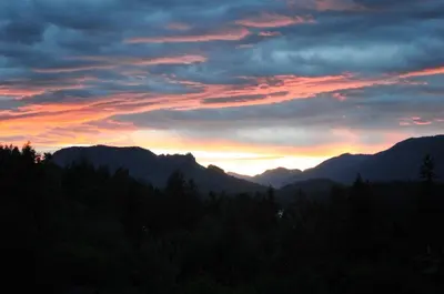 a sunset in the mountains with trees in the foreground at Valley View in Lake Cowichan