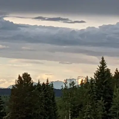 a sunset over the mountains with trees in the foreground at Willow Grove B&B Inn in Horsefly