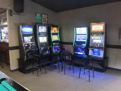 a row of slot machines in a room with stools at Battlefords Inn in North Battleford