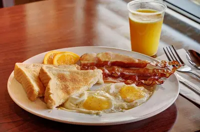 a plate of breakfast food with eggs bacon and orange slices at Lakeview Inns & Suites - Slave Lake in Slave Lake
