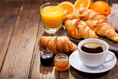 a table with a cup of coffee and croissants and orange juice at Pomeroy Inn and Suites Chetwynd in Chetwynd