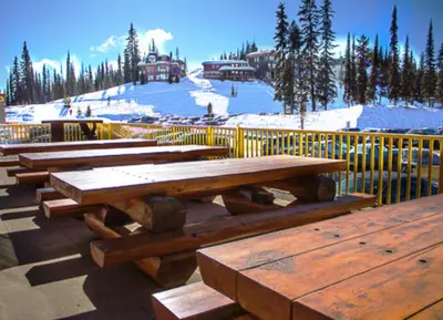 a group of wooden picnic tables in front of a snow covered mountain at The Bulldog Hotel in Silver Star