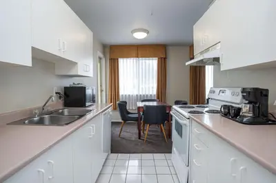 a kitchen with white cabinets and a table with chairs at Sandman Hotel & Suites Williams Lake in Williams Lake
