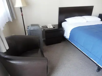 a bedroom with a bed and a chair and a phone at Stratford Motel in Whitehorse