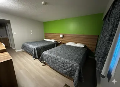 a room with two beds and a green wall at Quesnel Inn in Quesnel