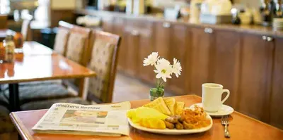 a table with a plate of food and a newspaper at Service Plus Inns & Suites Drayton Valley in Drayton Valley