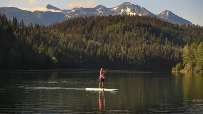 a woman standing on a paddle board in a lake at Tyax Lodge & Heliskiing in Gold Bridge