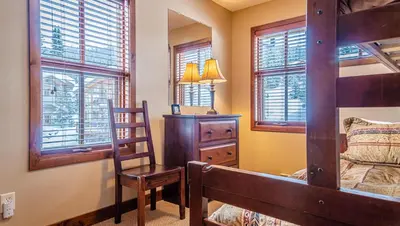 a bedroom with a bunk bed and a chair and windows at Woodhaven #36 By Bear Country in Sun Peaks