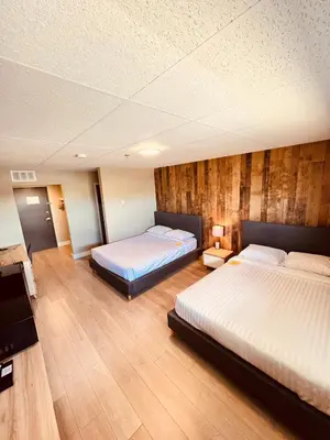 two beds in a room with wooden walls at Camrose Le Chateau Hotel in Camrose