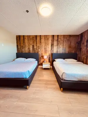 two beds in a room with wooden walls at Camrose Le Chateau Hotel in Camrose