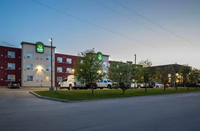 a parking lot with a building with green signs on it at Quality Inn & Suites in Whitecourt