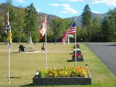 three flags in a park with flowers in the grass at Mountain Springs Motel & RV Park in Barrière