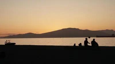 a group of people sitting on the beach at sunset at HI Vancouver Jericho Beach - Hostel in Vancouver