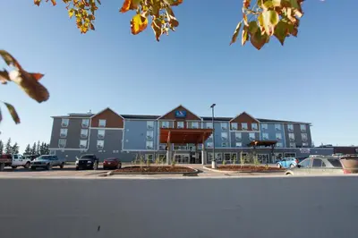 a large building with cars parked in a parking lot at Pomeroy Inn & Suites at Olds College in Olds