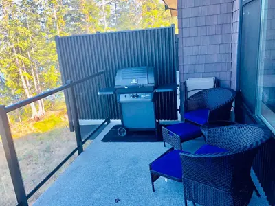 a patio with chairs and a grill on a porch at Sandy Feet Retreat Port Renfrew- Oceanfront 2BR modern cottage in Port Renfrew