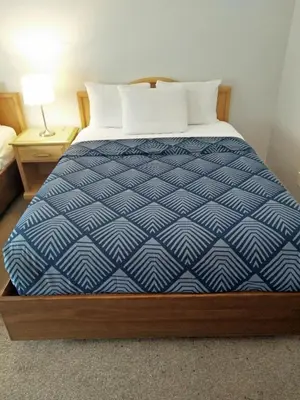 a bed with a blue comforter and white pillows at Sundowner Motel in Cache Creek